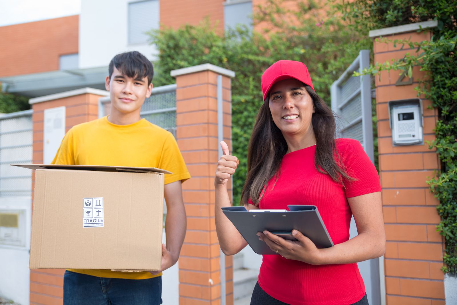 Una repartidora con gorra roja sonríe junto a un joven que lleva una caja
